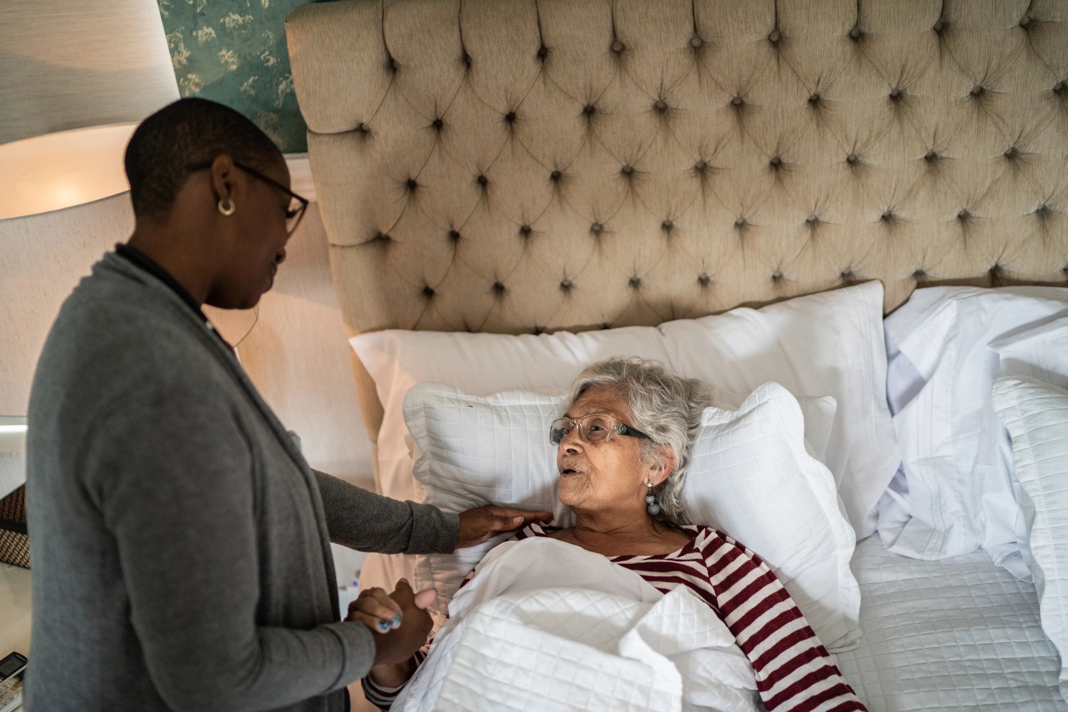 Nurse supporting an older woman resting in bed at home